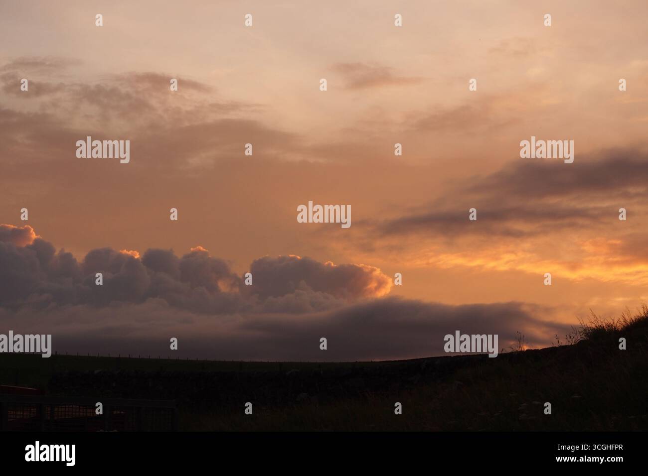 Un tramonto sulle fattorie costiere di Islay, Ebridi interne, Scozia, Regno Unito, che mostra le minacciose nuvole di pioggia che si riuniscono nel bagliore dorato Foto Stock