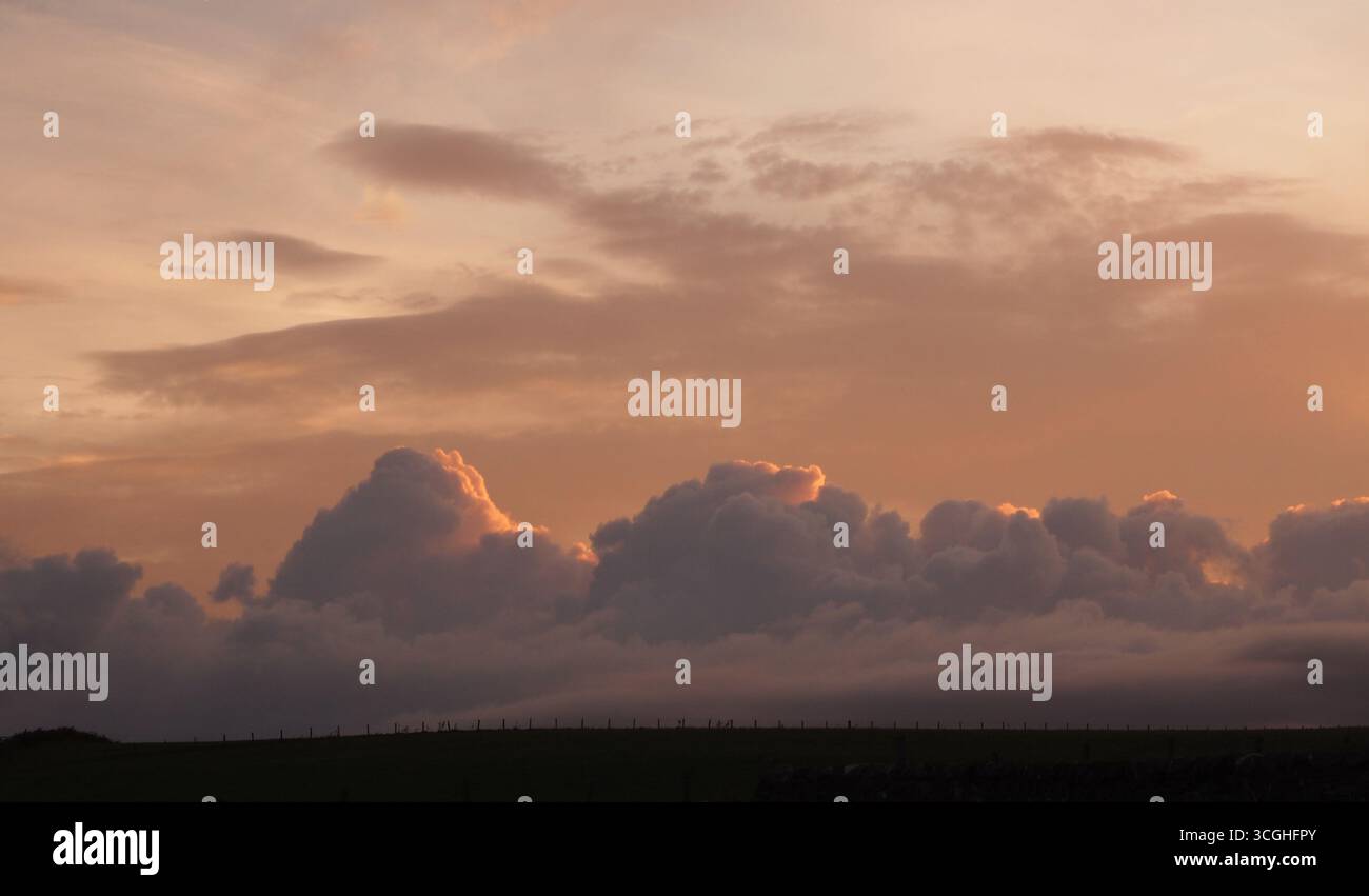 Un tramonto sulle fattorie costiere di Islay, Ebridi interne, Scozia, Regno Unito, che mostra le minacciose nuvole di pioggia che si riuniscono nel bagliore dorato Foto Stock
