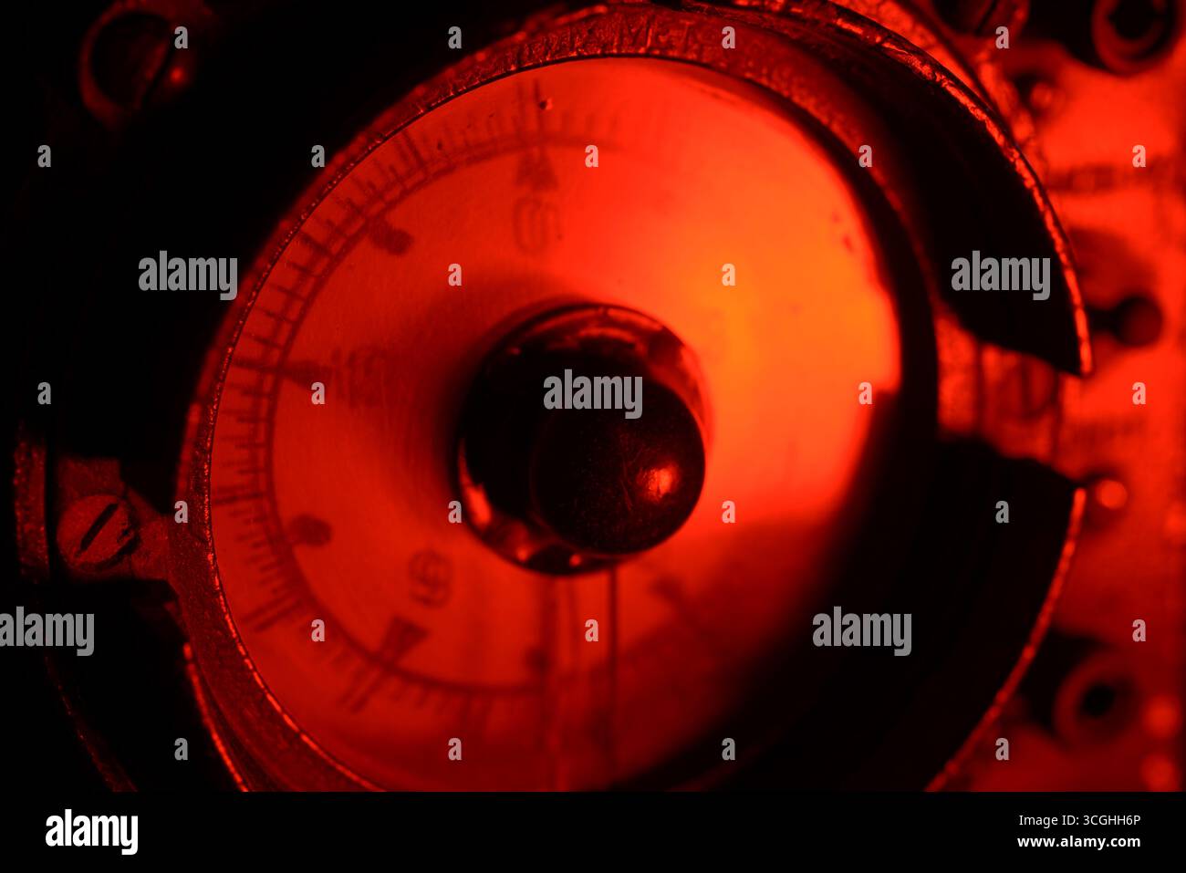 Primo piano di un altimetro analogico d'epoca che si illumina di rosso al buio, mostrando il design rétro degli strumenti aeronautici e i dettagli meccanici. Foto Stock