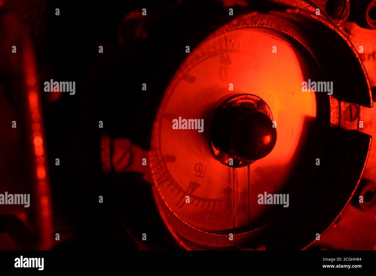 Primo piano di un altimetro analogico d'epoca che si illumina di rosso al buio, mostrando il design rétro degli strumenti aeronautici e i dettagli meccanici. Foto Stock