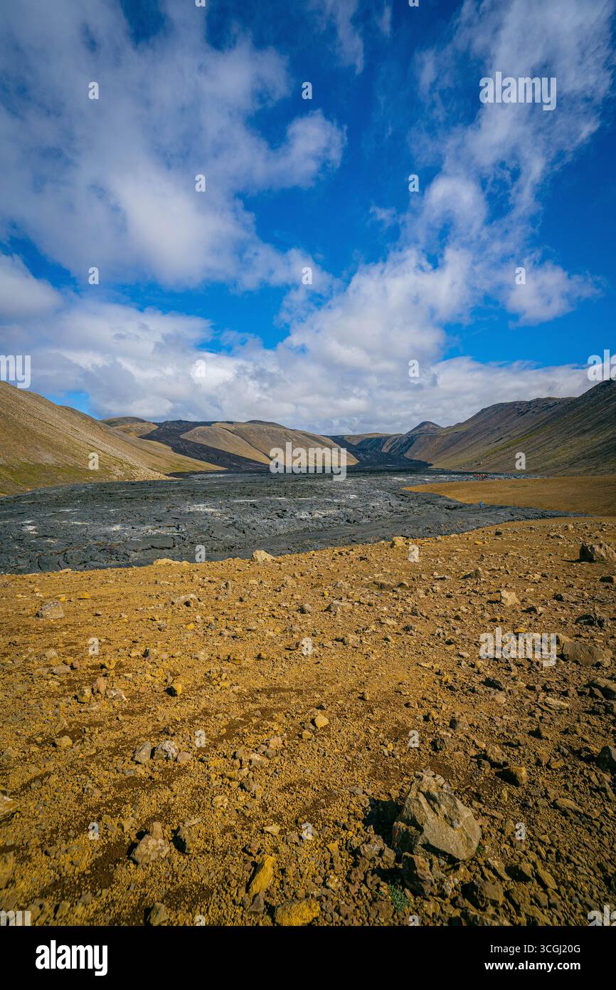 Una vallata islandese grezza dove le pendici vulcaniche dorate si incontrano con un fiume glaciale sotto cieli drammatici, incontaminata natura selvaggia nordica Foto Stock