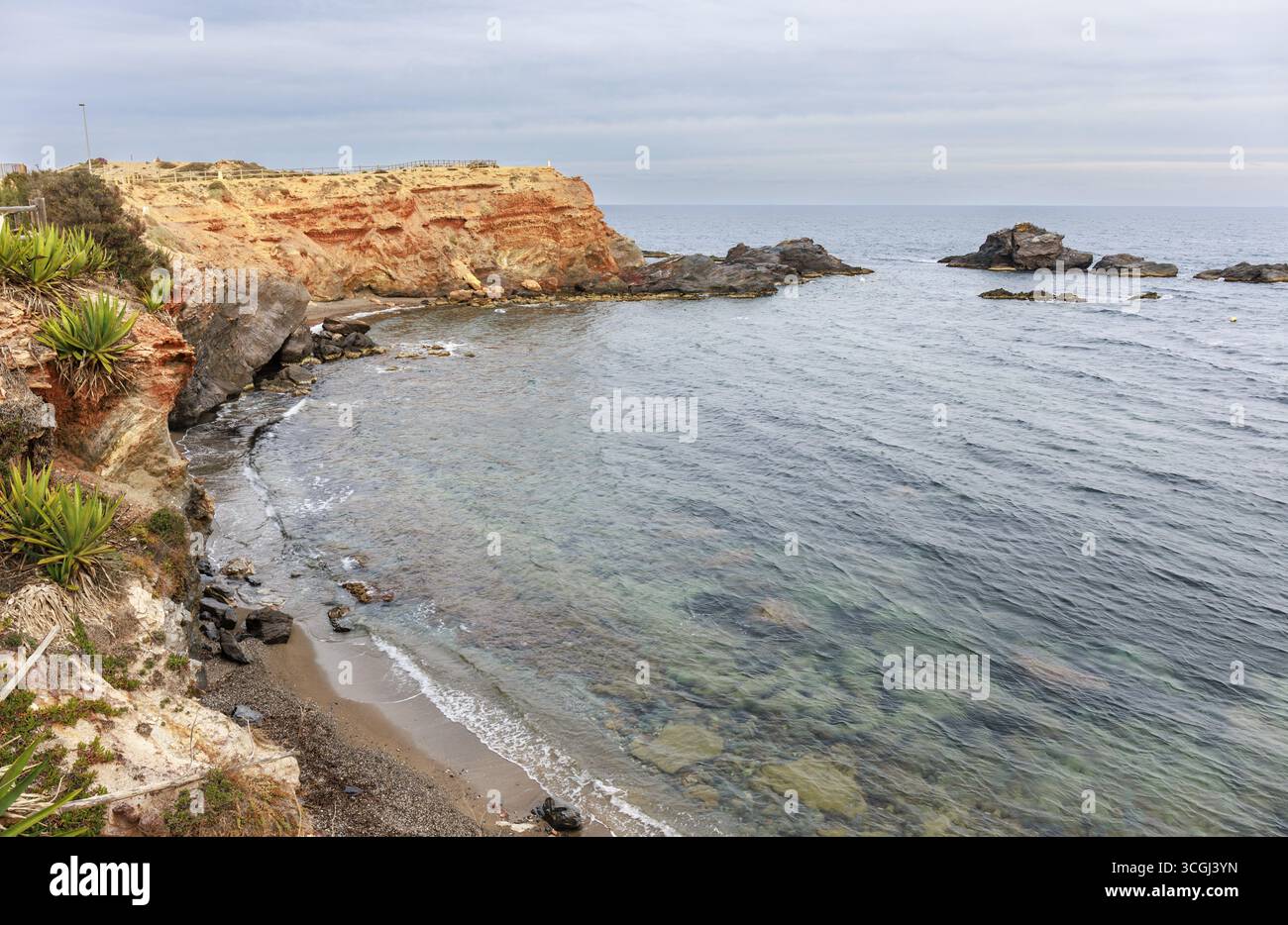 Vista panoramica della costa rocciosa di Cabo de Palos a Murcia con piccole insenature di acqua limpida sotto cieli nuvolosi Foto Stock