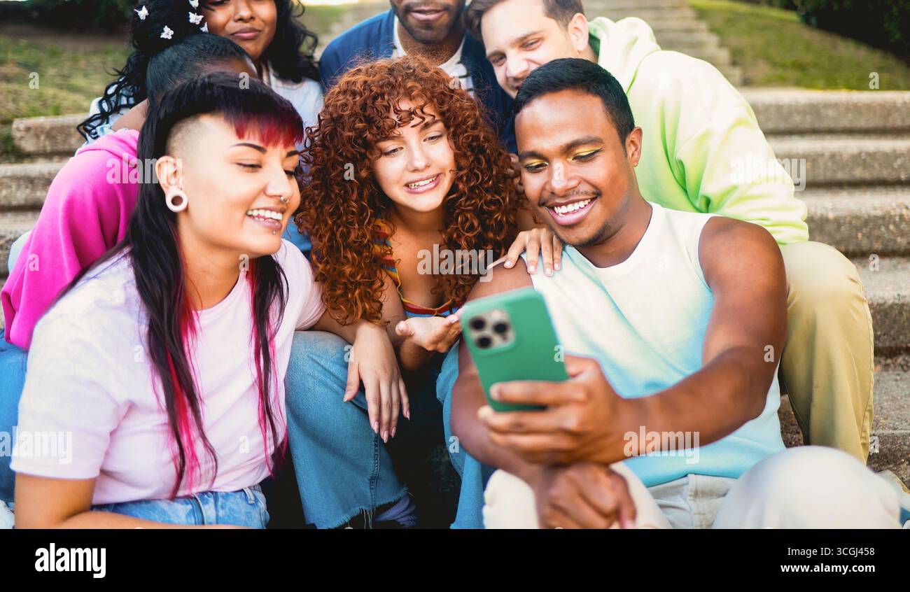 Giovani e diversi sorridono alla fotocamera del cellulare nel parco cittadino. Non binario africano che fa selfie con gli amici. Comunità LGBT Foto Stock