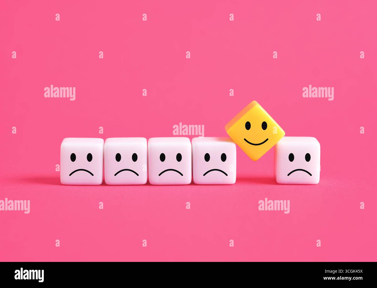 Cubo giallo felice che si distingue tra cubi bianchi tristi su sfondo rosa, simboleggiando il pensiero positivo o la soddisfazione del cliente. Foto Stock