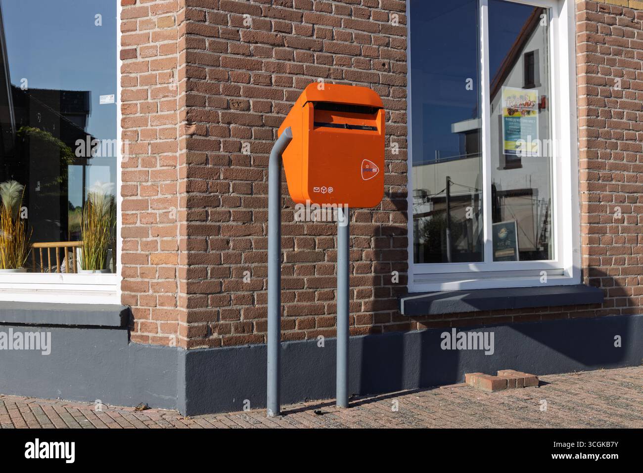 Un'iconica cassetta postale PostNL arancione, simbolo del servizio postale olandese, in piedi su un marciapiede all'esterno di un tradizionale edificio in mattoni. Nijmegen, Paesi Bassi. Foto Stock