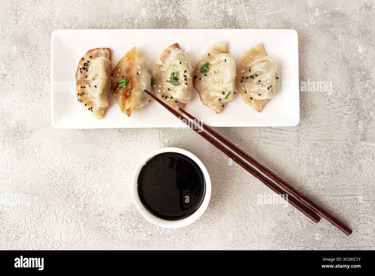 Gyoza gnocchi giapponesi, fritti, con salsa, cipolla verde e semi di sesamo, colore naturale, sfondo chiaro Foto Stock