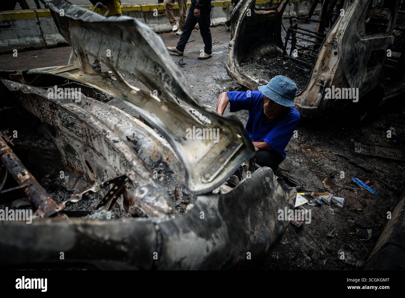 I residenti rimuovono parti di un'auto bruciata durante una protesta davanti al quartier generale della Mobile Brigade a Kwitang, nel centro di Giacarta, giovedì (28 agosto, Foto Stock