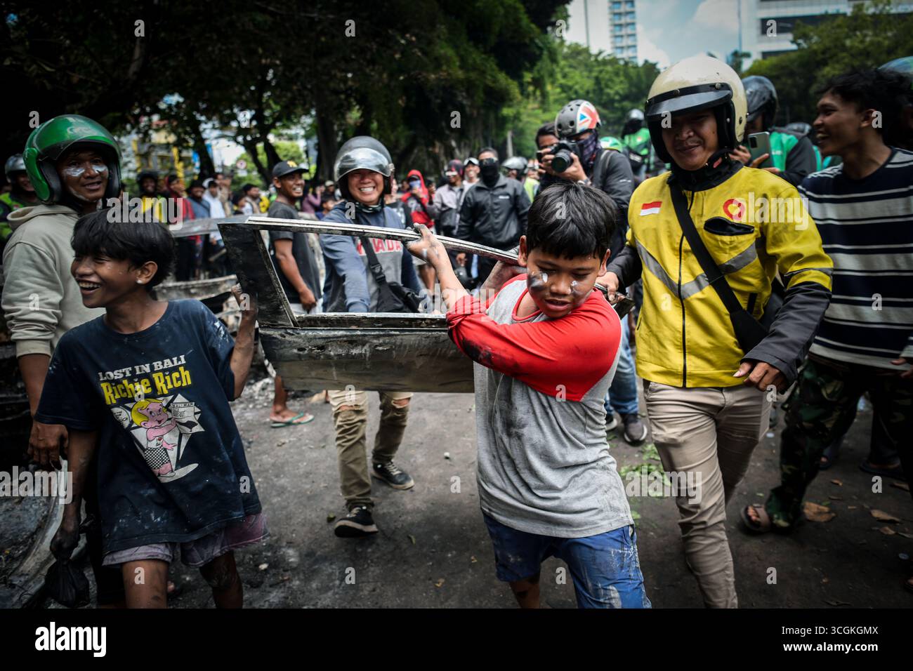 I residenti rimuovono parti di un'auto bruciata durante una protesta davanti al quartier generale della Mobile Brigade a Kwitang, nel centro di Giacarta, giovedì (28 agosto, Foto Stock