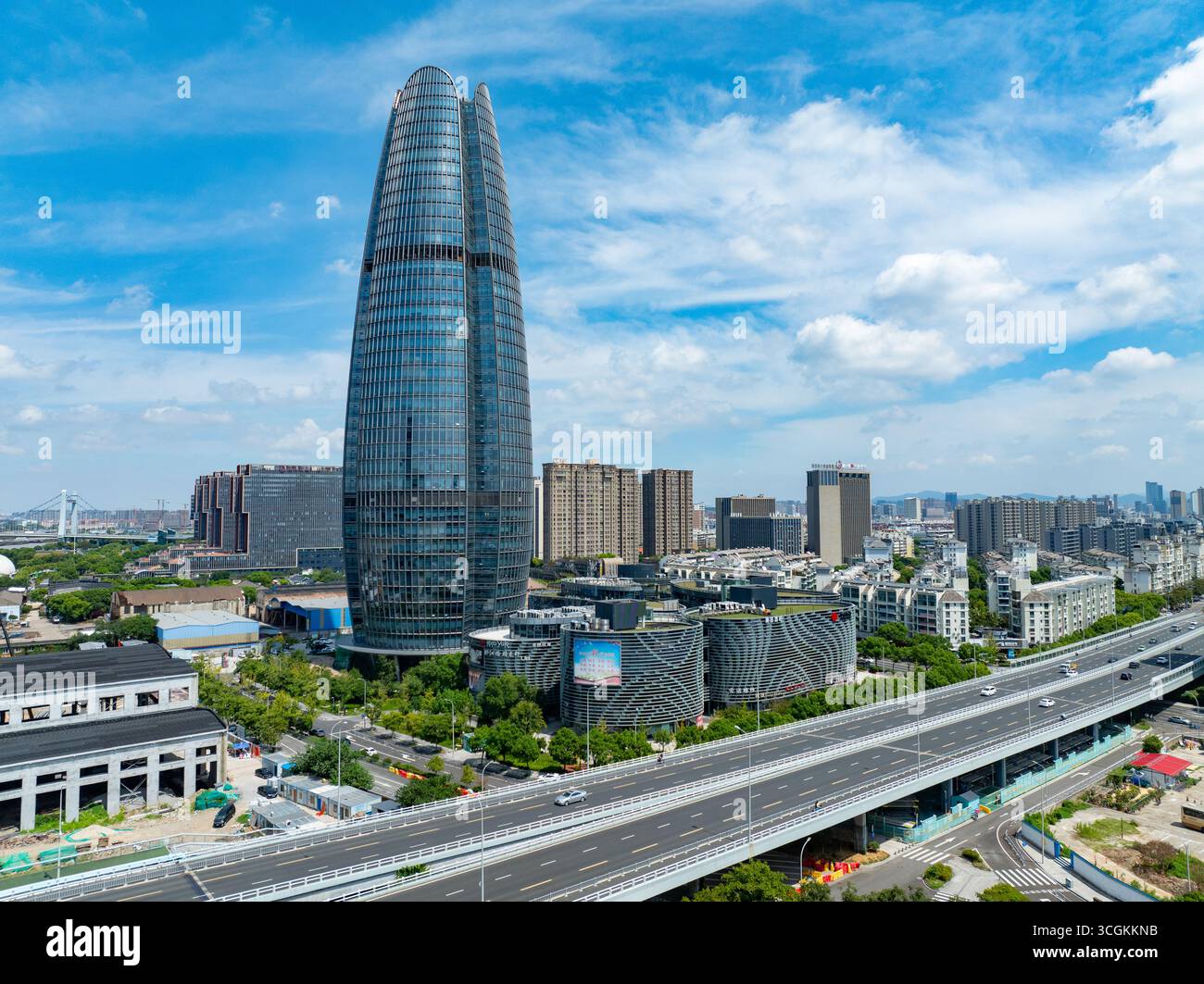Moderno paesaggio urbano con un grattacielo di vetro che si erge sopra gli edifici della città e una trafficata autostrada a più corsie. Foto Stock