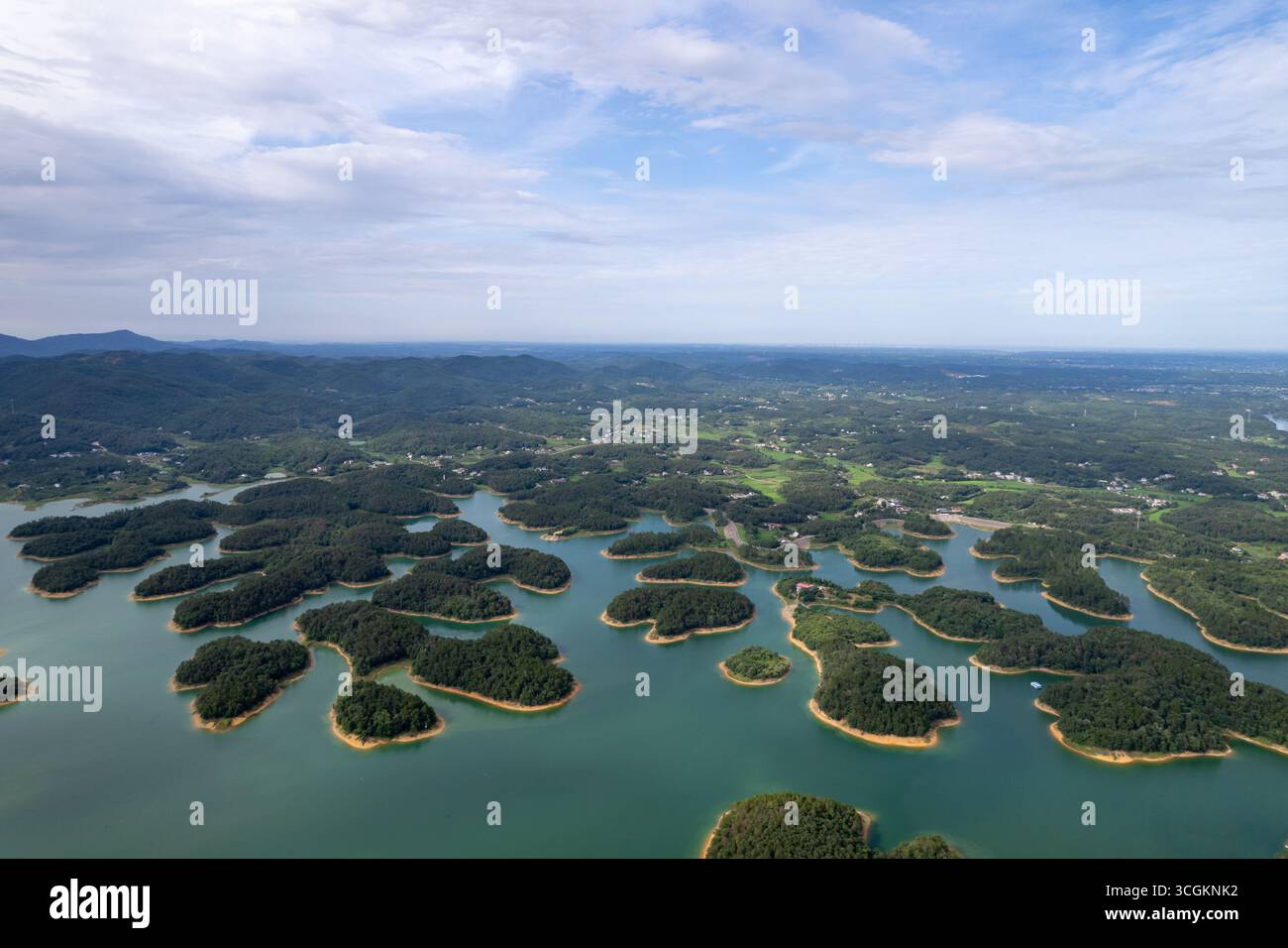 Un'ampia vista mostra molte piccole isole ricoperte di alberi che punteggiano un grande corpo di acque blu calme sotto un cielo parzialmente nuvoloso. Le isole sono sparse Foto Stock