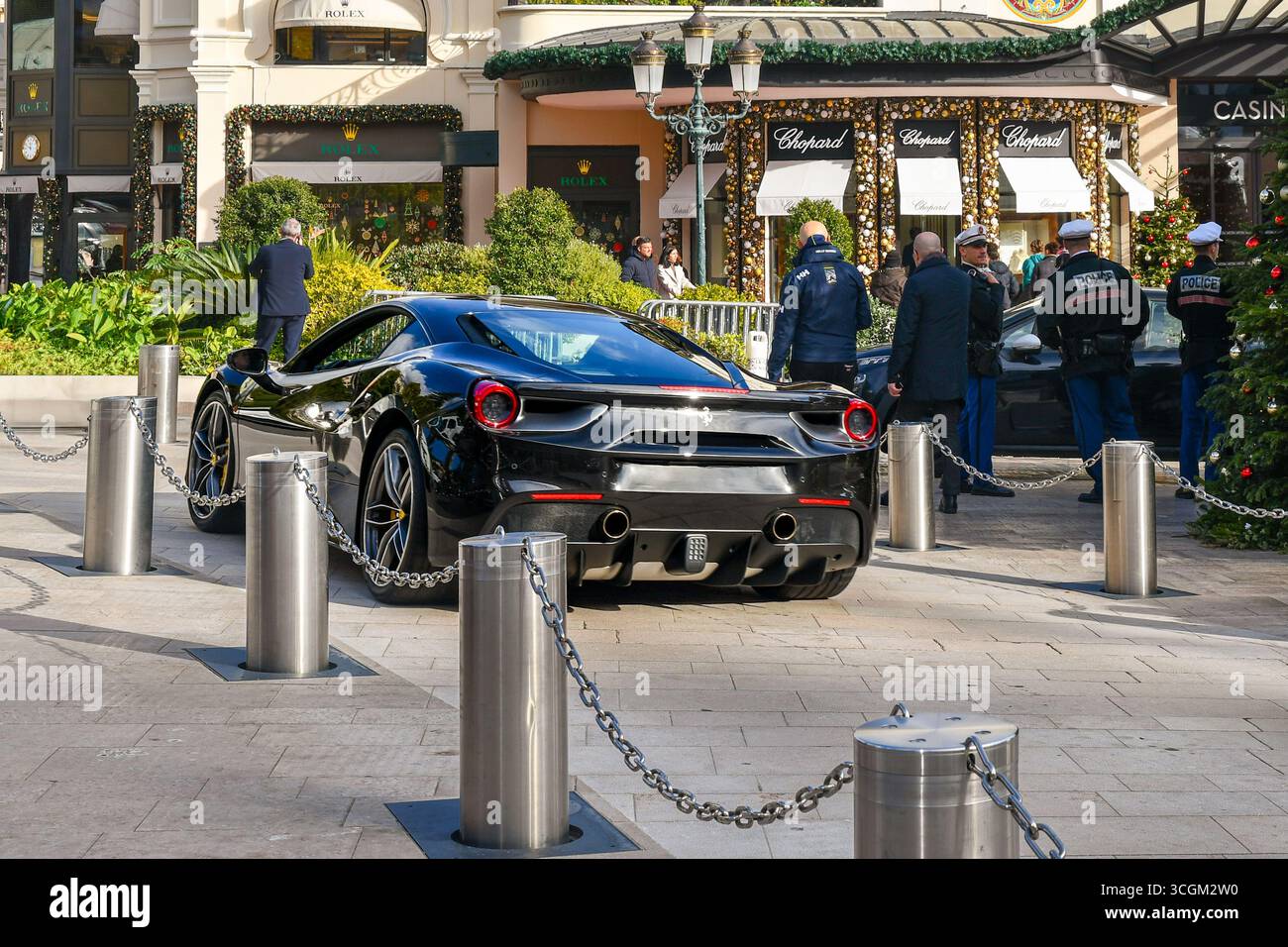Un'elegante Ferrari 488 GTB nera che passa di fronte al casinò slot-machine, con agenti di polizia e decorazioni natalizie, Monte Carlo, Monaco Foto Stock