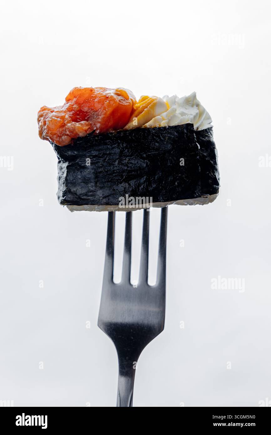 Un pezzo di sushi appeso su una forchetta su sfondo bianco Foto Stock