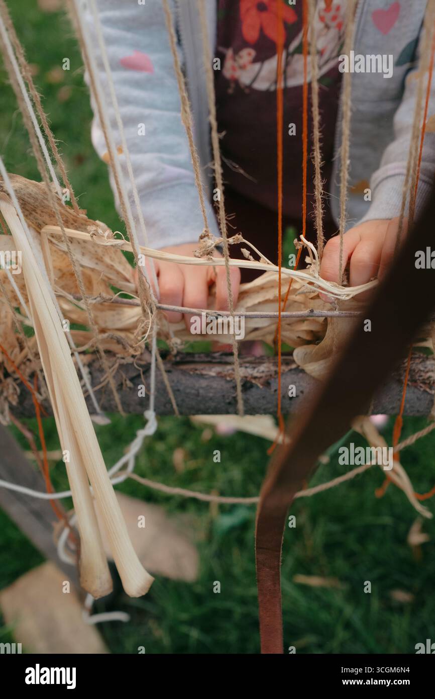 Tessitura in età prescolare di materiali naturali su telai esterni in autunno Foto Stock