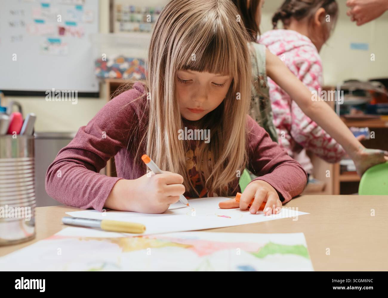 Ragazza in età prescolare che disegna con pennarelli a tavola in classe Foto Stock