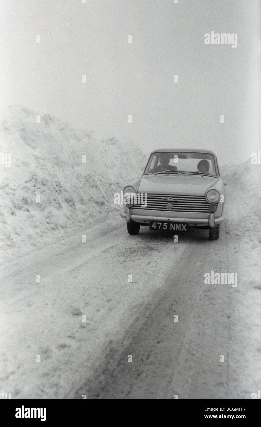 1960, storica, vista frontale di un'auto Austin A40 Farina a 3 porte dell'epoca su una stretta pista innevata in un tour del continente. Papà alla guida, figlia seduta accanto a lui. Con un design italiano di Battista Farina e in produzione tra il 1958 e il 1967 dalla British Motor Corporation (BMC), l'Austin A40 fu l'ultima delle molte vetture con questo nome. Foto Stock