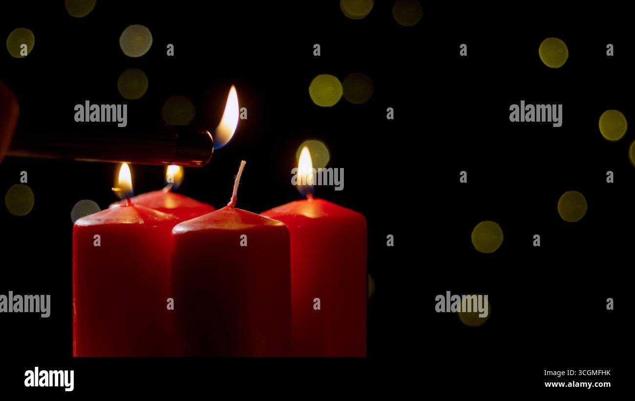 Una mano accende una candela rossa circondata da luci bokeh, creando un'atmosfera calda e accogliente durante la serata. Foto Stock