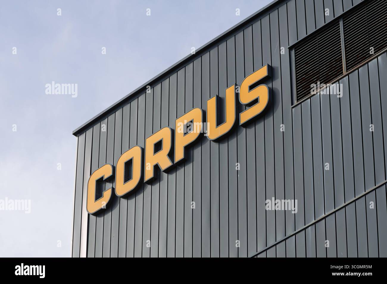 Il moderno edificio 'CORPUS', con la sua distintiva scritta arancione su una elegante facciata grigia, si erge sotto un cielo dinamico. Rappresenta l'innovazione, Foto Stock