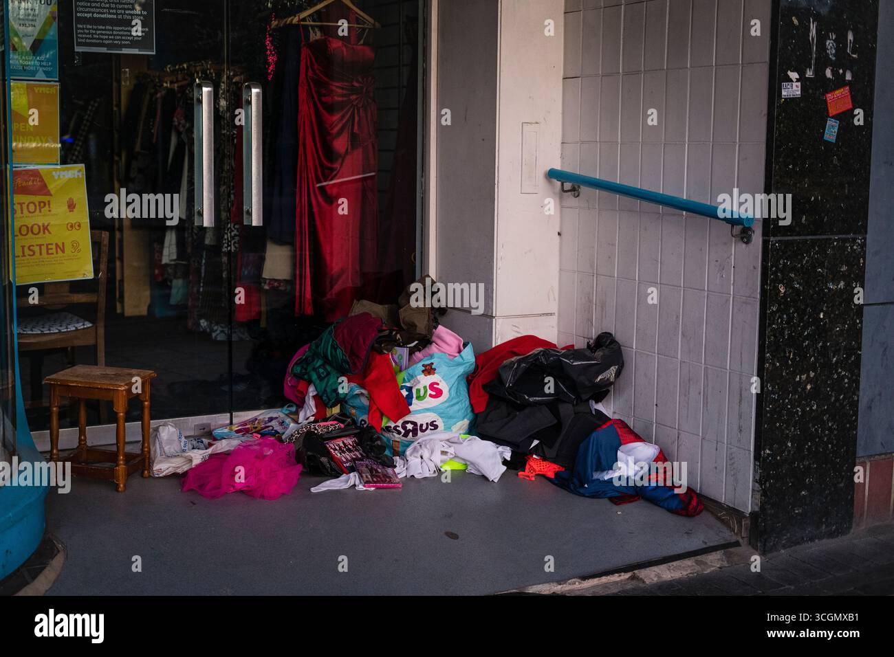 L'ingresso di un negozio di beneficenza chiuso con una donazione rimasta e alcuni oggetti spazzatura gettati e gettati fuori dal negozio. Foto Stock