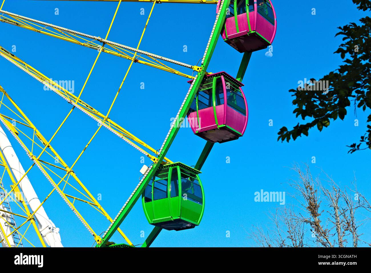 Foto ravvicinata delle gondole verdi e rosa di una ruota panoramica gigante con la luna sullo sfondo. Foto Stock