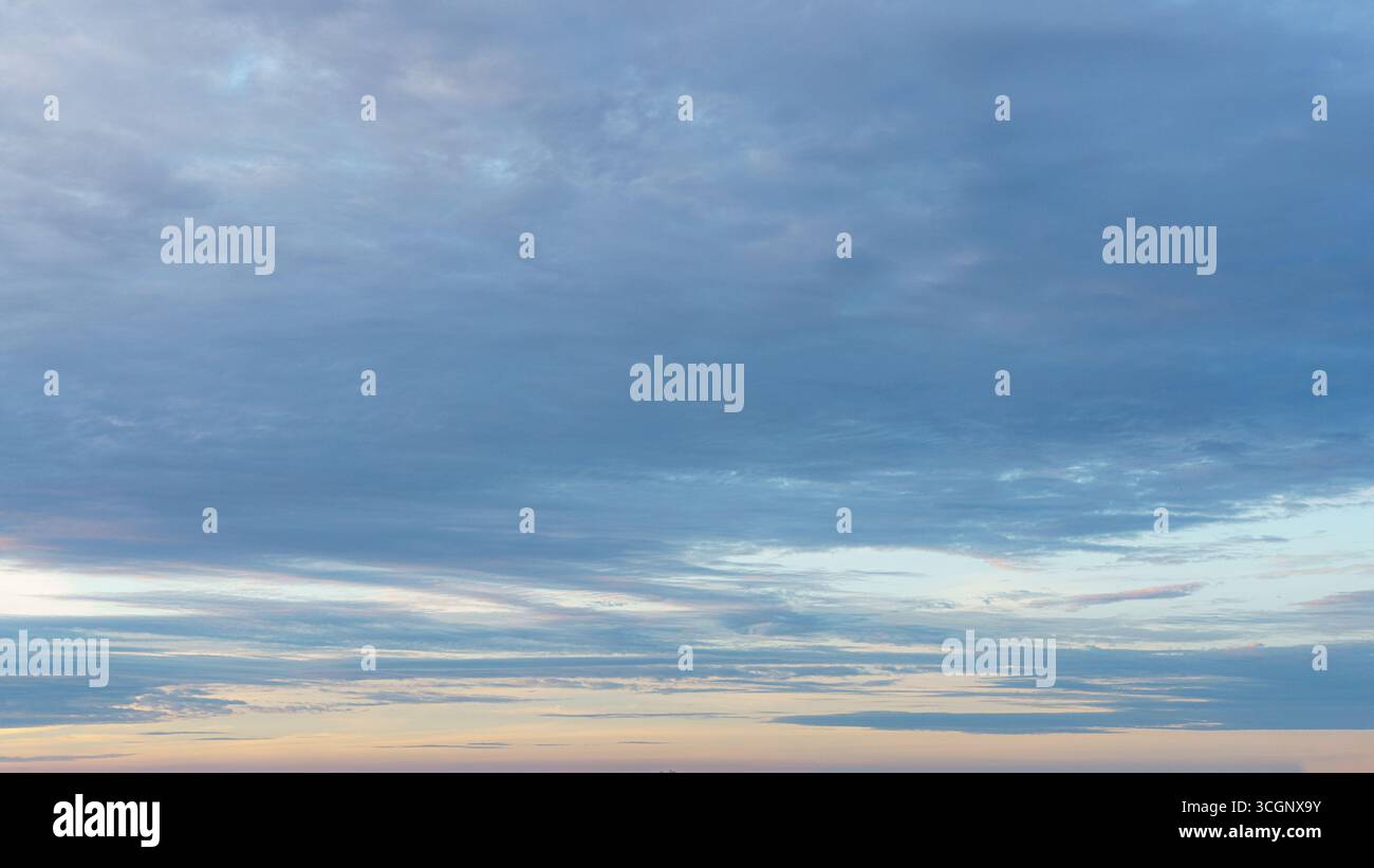 Le nuvole altostrato riempiono il cielo mattutino con tonalità blu e lavanda. Foto Stock