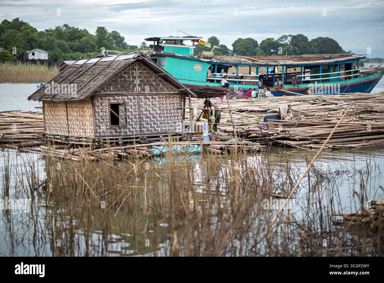 Ayeyarwady River Floating House Bamboo Logs MANDALAY Myanmar // MANDALAY, Myanmar — Una tradizionale casa galleggiante sul fiume Ayeyarwady (conosciuta anche come Irrawaddy), costruita con tronchi di bambù, si trova sul fiume a Mandalay. La casa presenta pareti di bambù intrecciate ed è circondata da numerosi tronchi di bambù, probabilmente utilizzati per i materiali da costruzione o il trasporto. Queste strutture galleggianti sono comuni lungo il fiume Ayeyarwady, che è il più lungo e importante corso d'acqua commerciale del Myanmar. Il fiume funge da arteria vitale per il commercio, i trasporti e la vita quotidiana di comunità come quelle Foto Stock