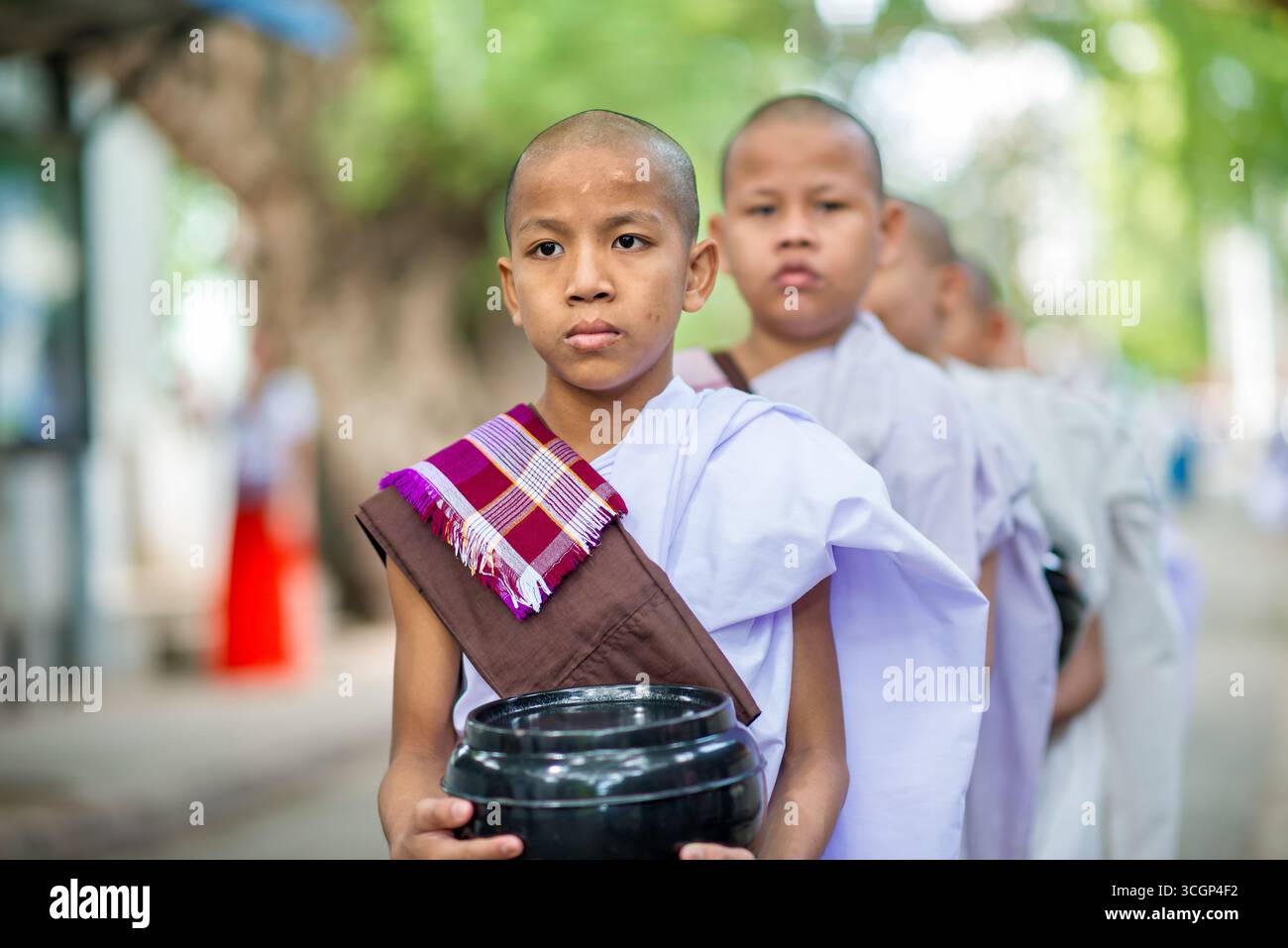Linea pranzo dei novizi del monastero di Mahagandayon Mandalay Myanmar // MANDALAY, Myanmar - i monaci buddisti novizi si schierano per il pranzo al monastero di Mahagandayon (noto anche come monastero di Mahagandayone) a Mandalay, Myanmar. Il monastero di Mahagandayon è uno dei più grandi e rispettati college monastici del Myanmar, sede di migliaia di monaci e novizi. Il pranzo giornaliero, solitamente servito intorno alle 10:30, è un evento significativo in cui la comunità monastica si riunisce per il pasto principale della giornata. Questo rituale quotidiano mette in evidenza la vita disciplinata del Buddhismo Theravada praticato in Myanmar, enfatizzando la communa Foto Stock