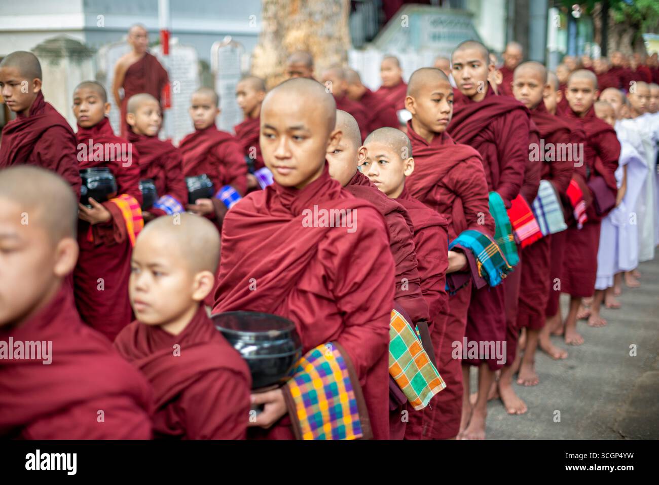 I novizi del monastero di Mahagandayon si allineano per il pranzo Mandalay Myanmar // MANDALAY, Myanmar - i novizi buddisti si allineano per il pranzo al monastero di Mahagandayon, una delle più grandi università monastiche del Myanmar. Questo rituale giornaliero coinvolge migliaia di monaci e novizi che partecipano a una processione silenziosa delle elemosine prima del loro pasto principale. Situato ad Amarapura, un'ex capitale reale vicino a Mandalay, il monastero è un importante centro per l'educazione monastica e lo studio del Buddhismo Theravada. Ospita migliaia di monaci e novizi, fornendo loro una formazione religiosa e un sostentamento quotidiano. I monas Foto Stock