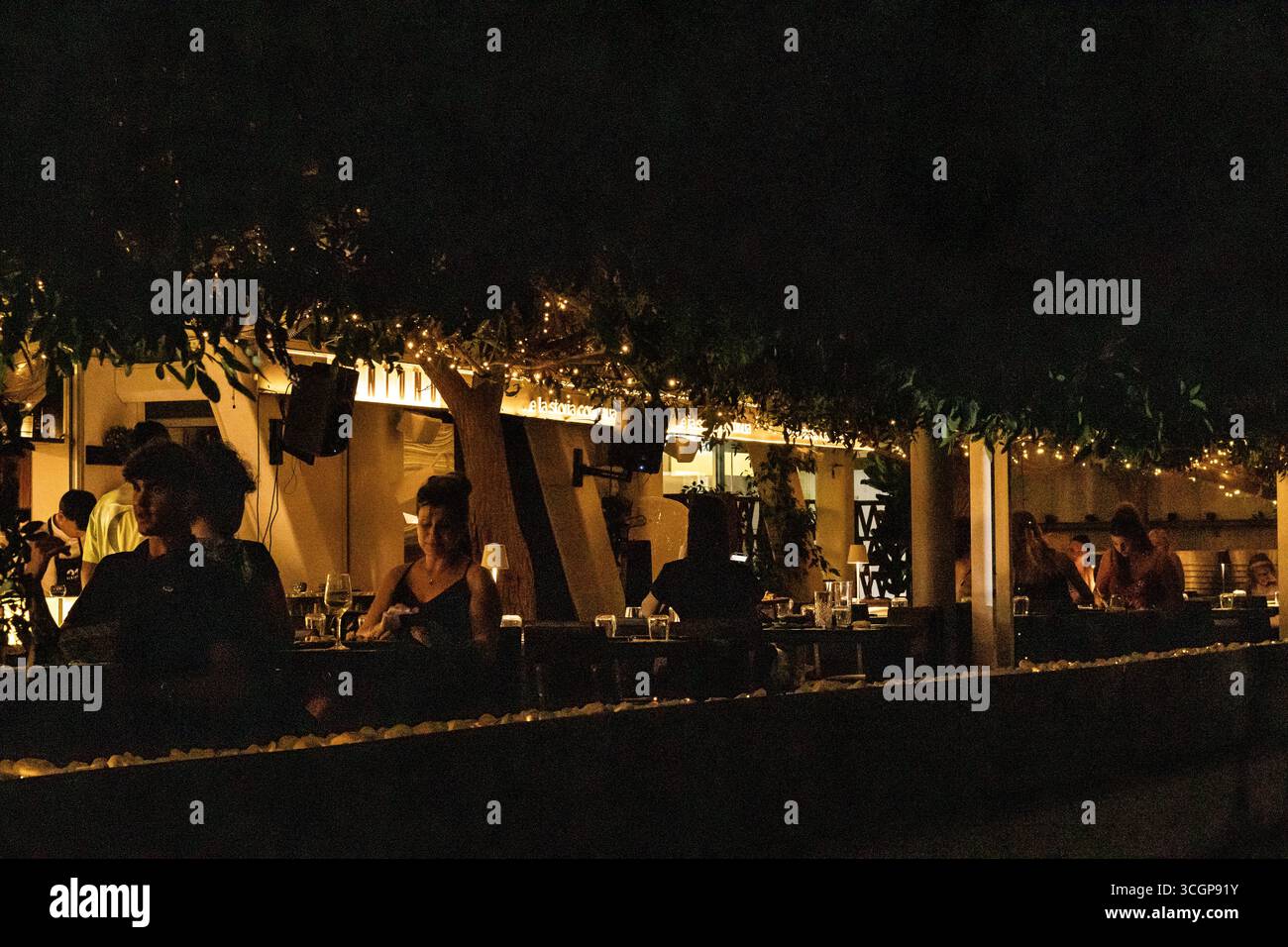 Un'incantevole zona pranzo all'aperto trasuda calore con le sue luci accese e l'atmosfera accogliente, adatta a godersi la vivace vita notturna o momenti intimi Foto Stock