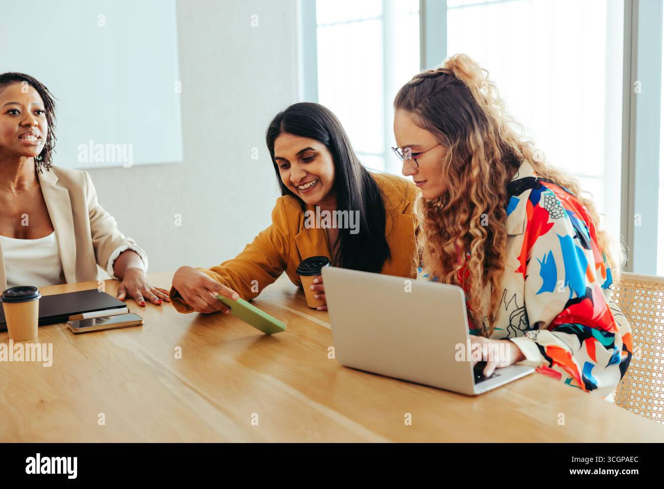 Gruppo di colleghi che collaborano durante una riunione di lavoro. Tre donne condividono idee mentre utilizzano un computer portatile e uno smartphone. L'ambiente d'ufficio Foto Stock