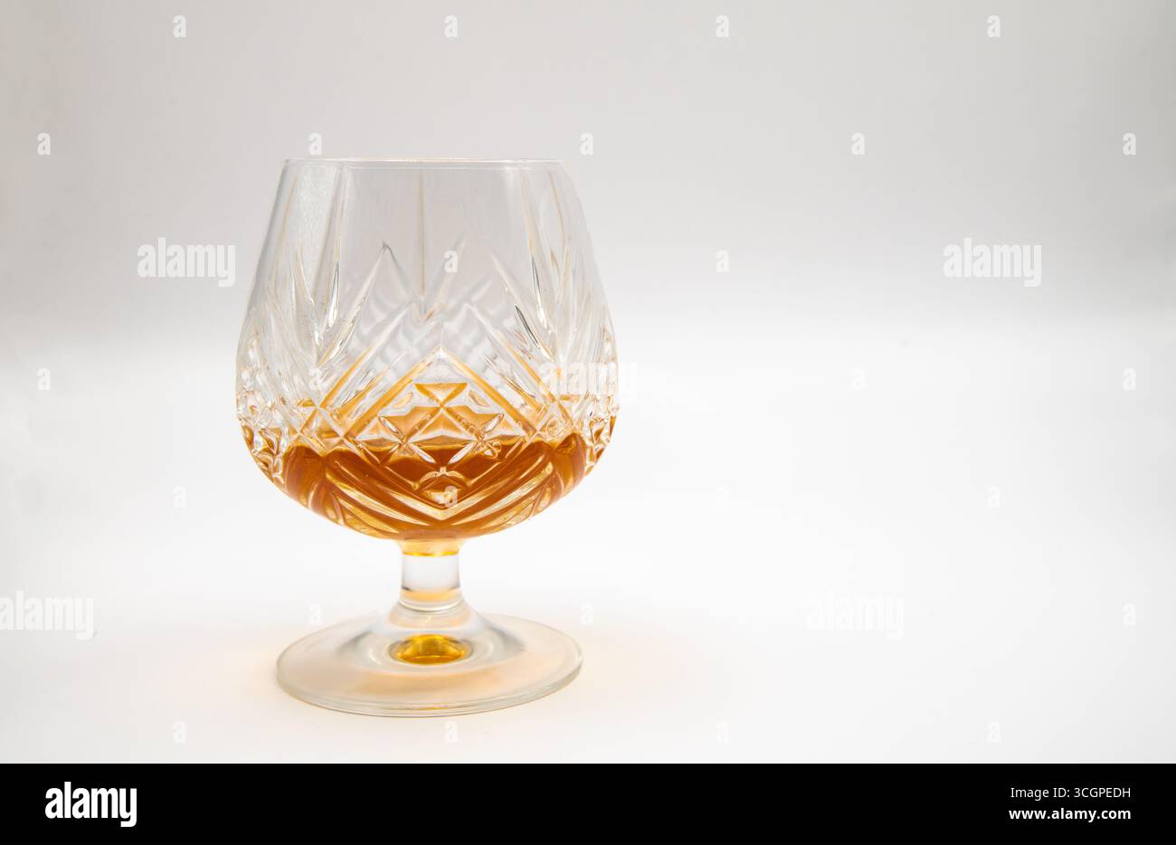 Taglia un bicchiere di brandy di cristallo riempito di brandy dorato su un semplice sfondo bianco, a simboleggiare l'eleganza, il lusso, gli spiriti raffinati e il bere sofisticato Foto Stock