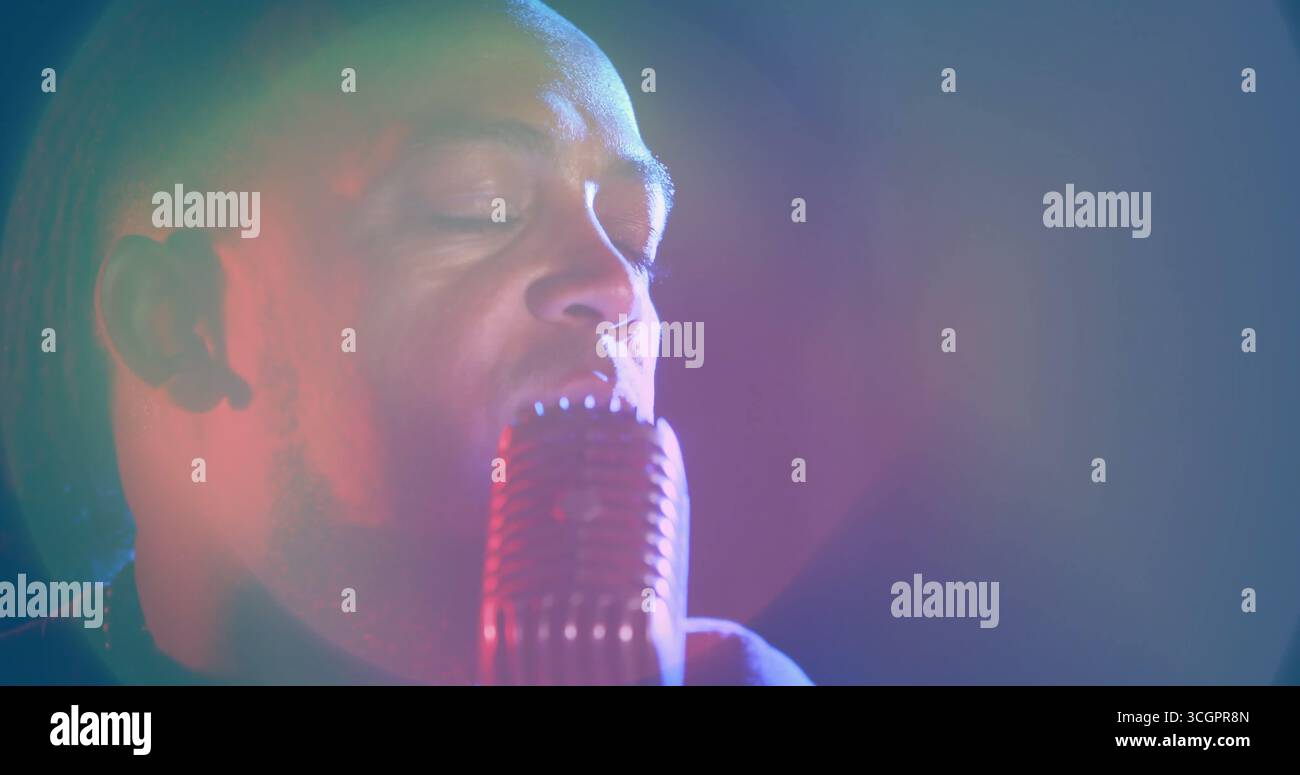 Cantante maschile che indossa una camicia scura e tiene il microfono retrò sul palco con faretti colorati Foto Stock