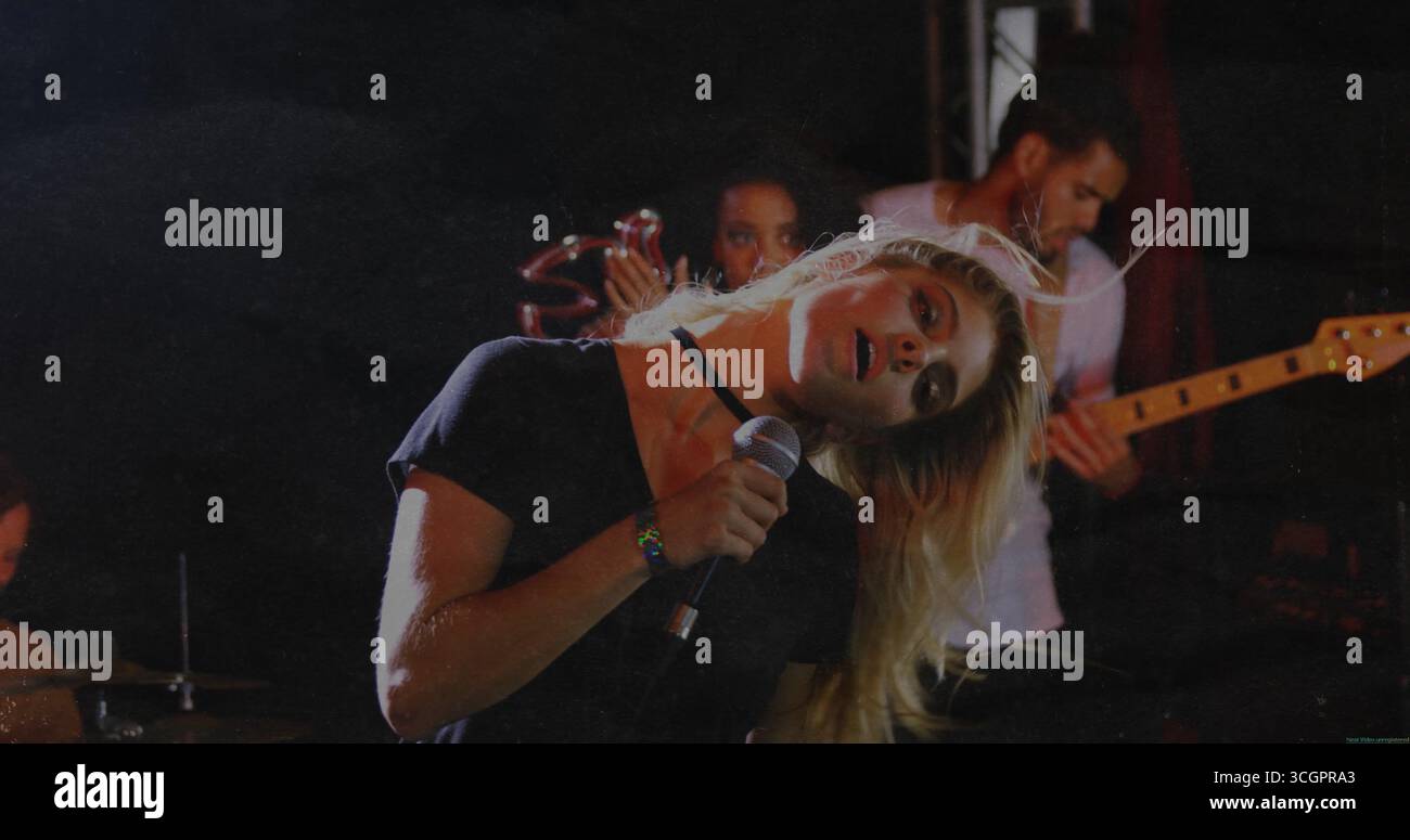 Cantante bionda pendente con microfono sul palco, con batteria, tamburello e basso Foto Stock