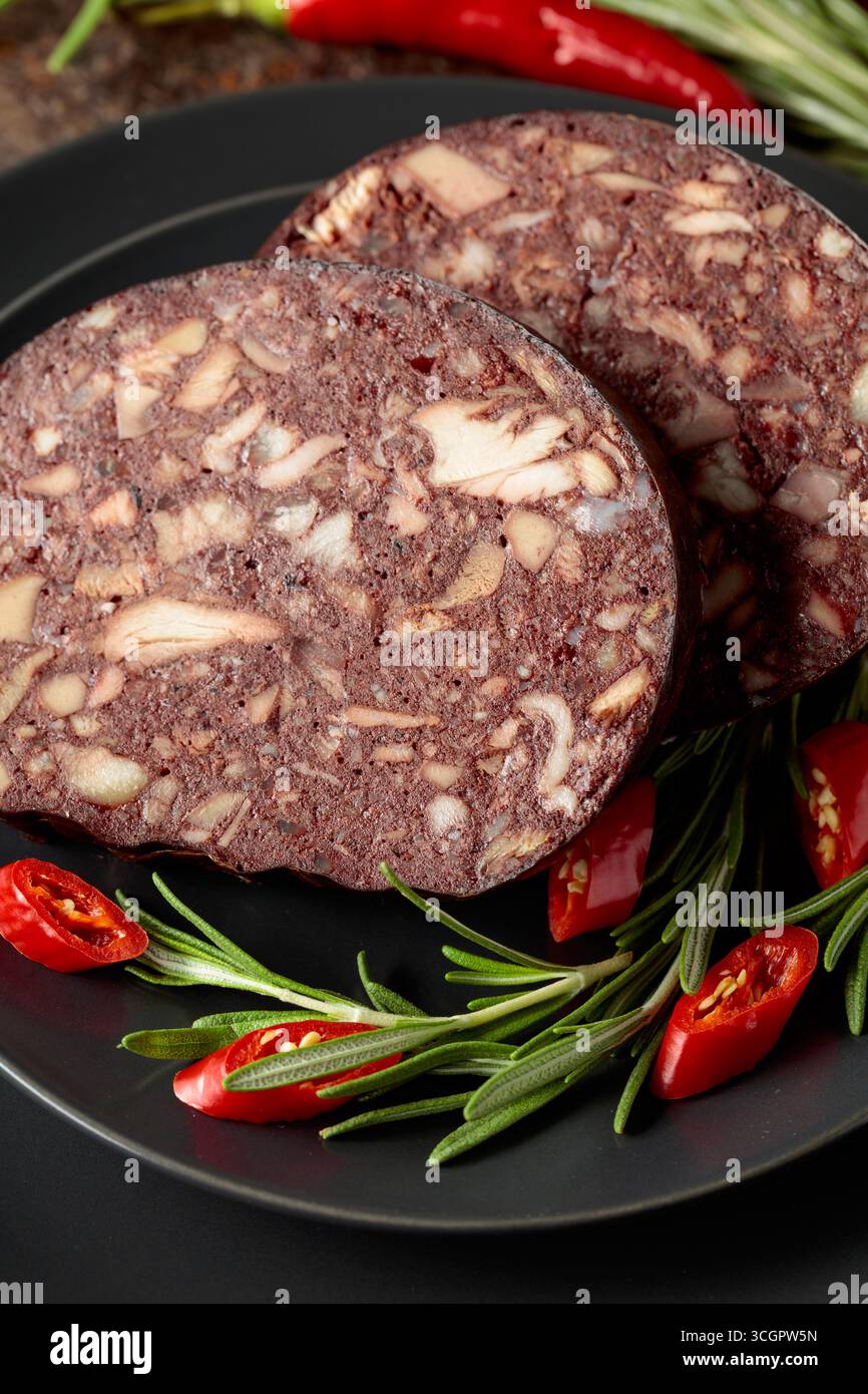 Salsiccia di sangue con frattaglie di carne accompagnata da rosmarino e pepe rosso su un piatto nero. Foto Stock