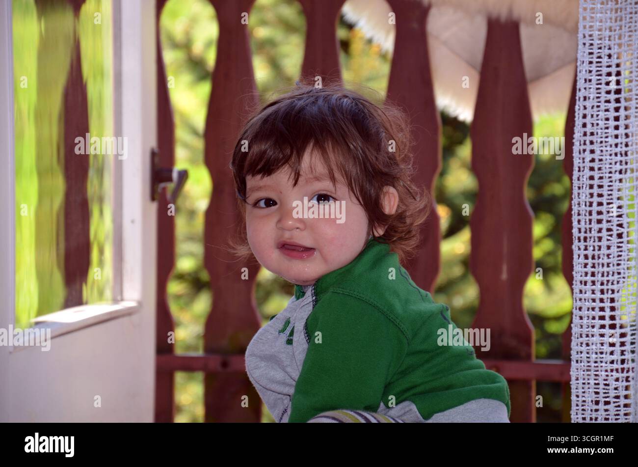 Un allegro bimbo di due anni mangia guardando direttamente l'obiettivo della fotocamera. Il bambino sorride con gioia, creando un momento naturale e caldo Foto Stock
