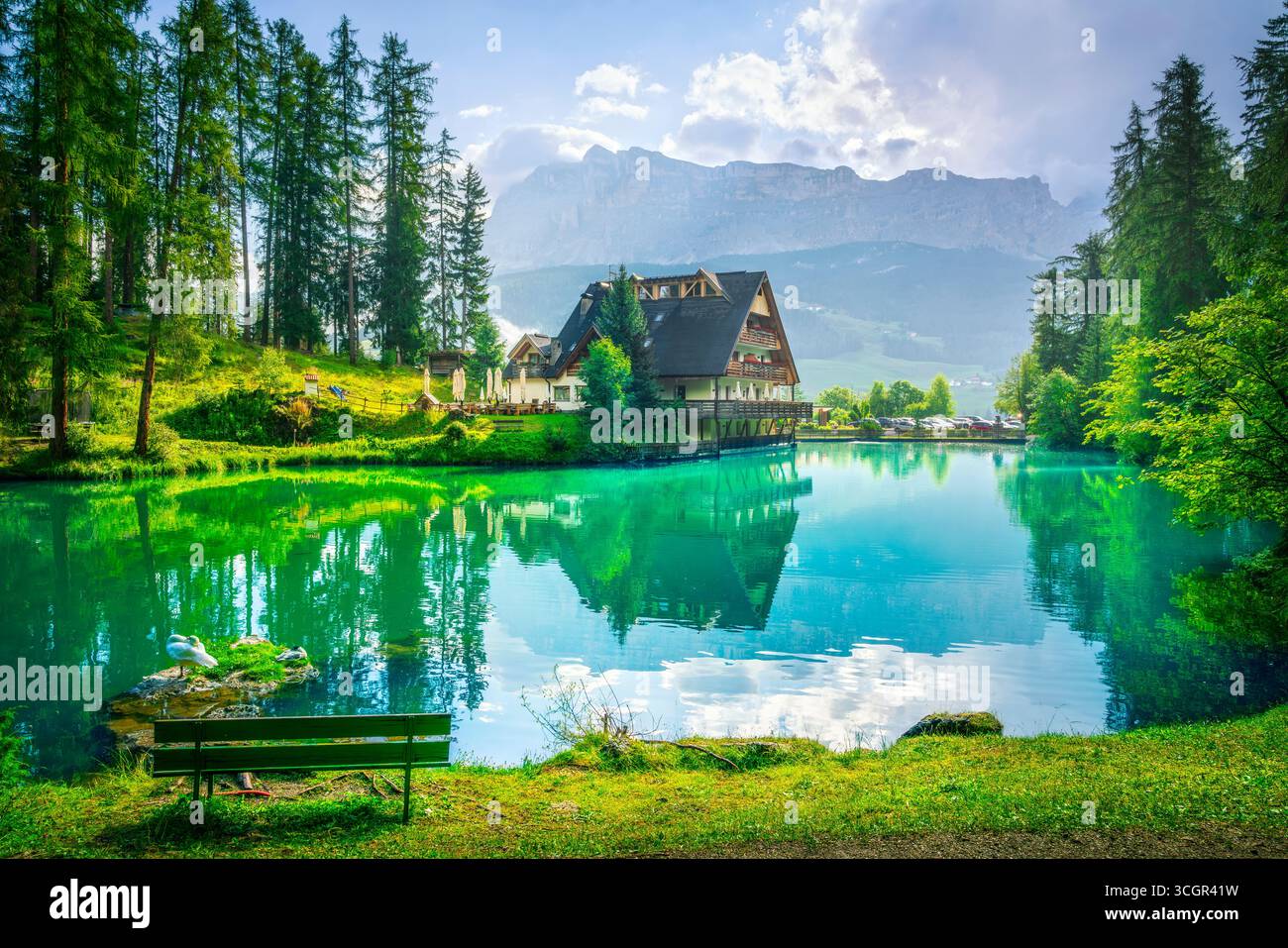 Lago panoramico Sompunt con acque cristalline color smeraldo che riflettono le tradizionali case alpine e la lussureggiante foresta nella valle di Badia, sito UNESCO delle Dolomiti, Sout Foto Stock