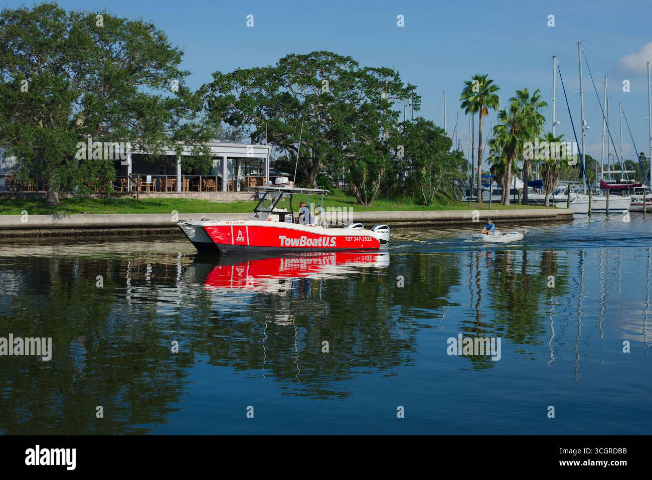 Red Boat e Small Dinghy sul lungomare con porticciolo e palme. Uso editoriale solo 29 agosto 2025 Gulfport, FL USA. Imbarcazione rossa per assistenza marina accesa Foto Stock