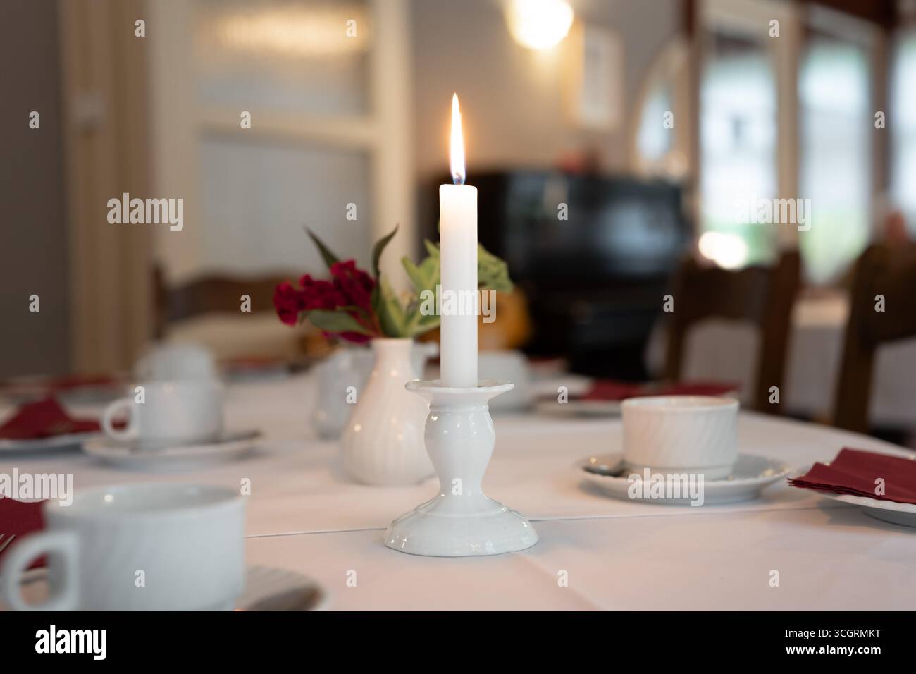 Scintillante candela su un tavolo da cena. Luce elegante in una location per eventi. Festeggiamo un compleanno, un matrimonio o un anniversario con la famiglia. Decorata in modo accogliente. Foto Stock