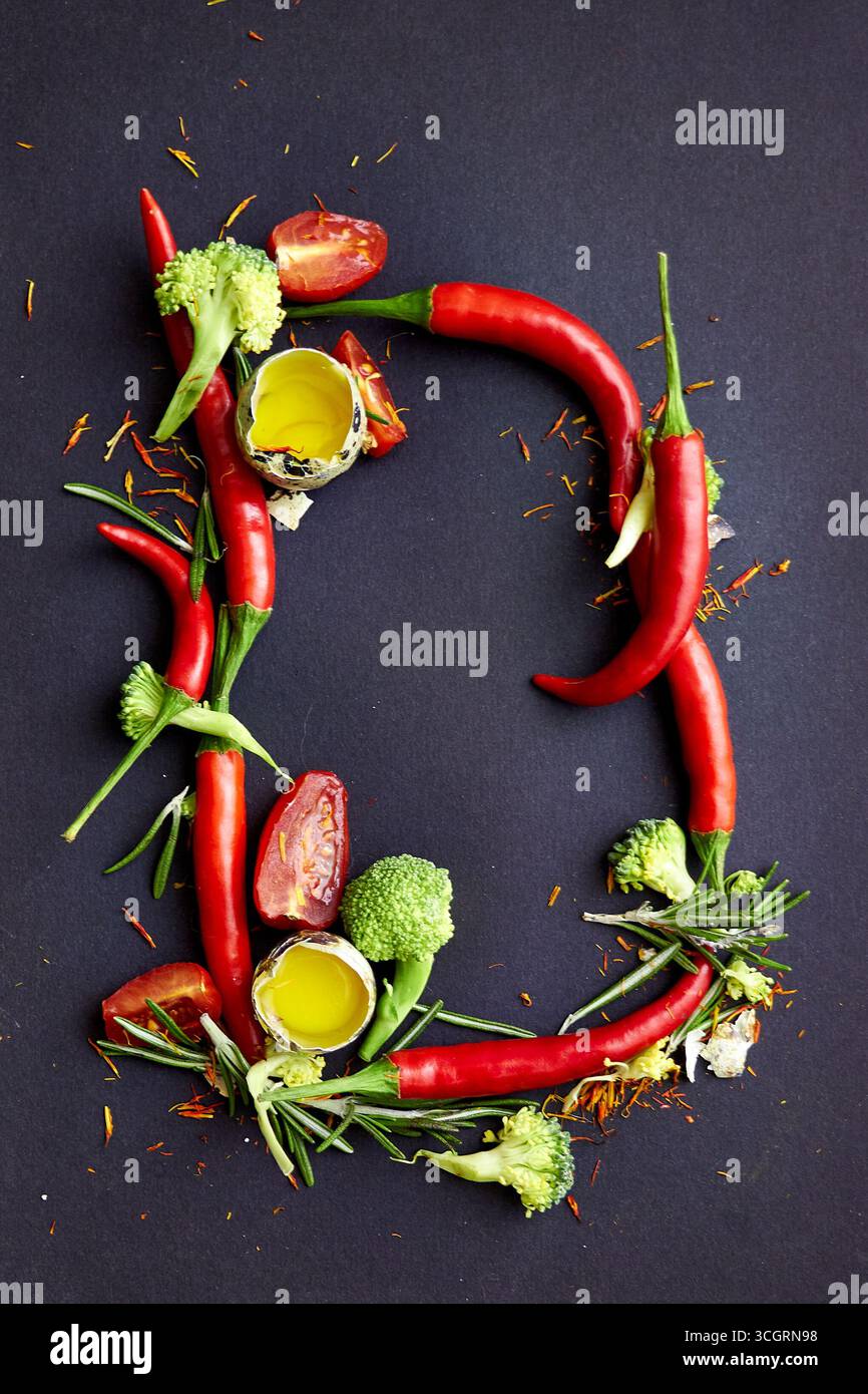Lettera creativa D composta da peperoncino, broccoli, rosmarino, pomodoro e olio d'oliva su sfondo scuro. Tipografia artistica del cibo per mangiare sano Foto Stock