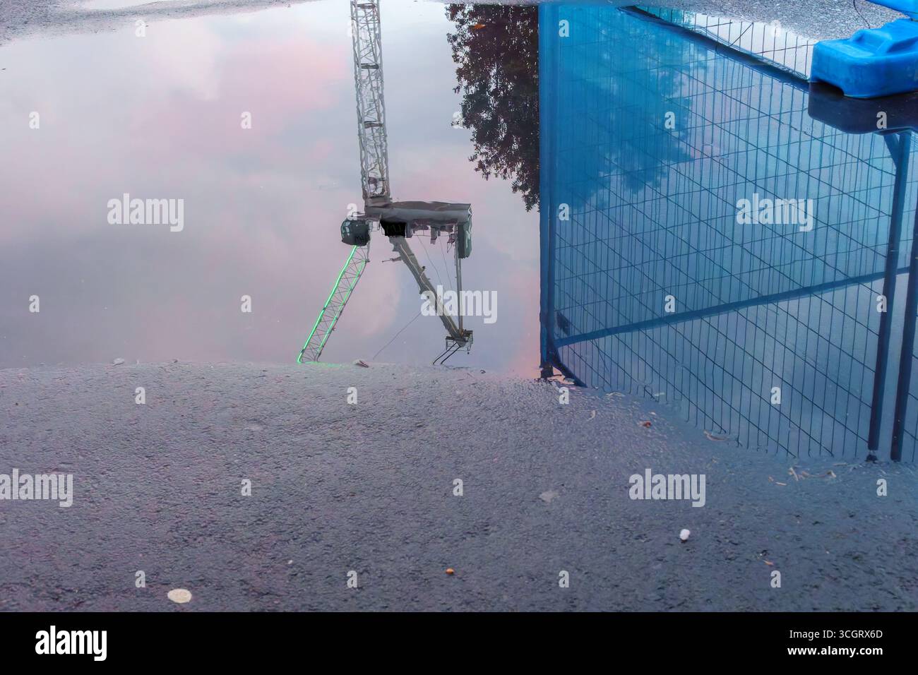 Scena di strada con riflesso del cantiere e gru in una pozzanghera di acqua piovana sulla strada Foto Stock