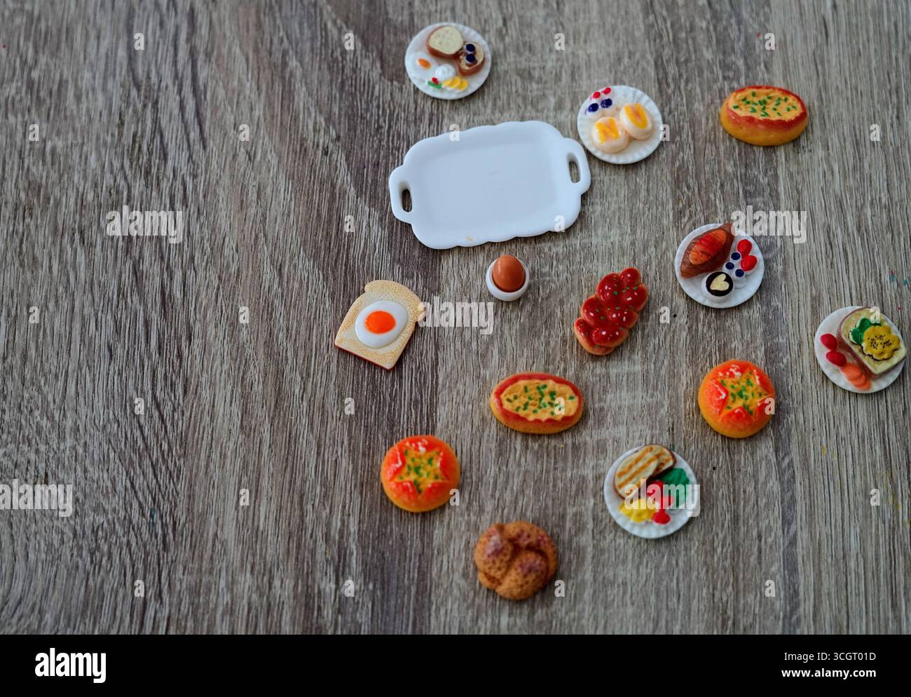 Una deliziosa collezione di prodotti alimentari in miniatura esposti su un tavolo di legno per la colazione Foto Stock