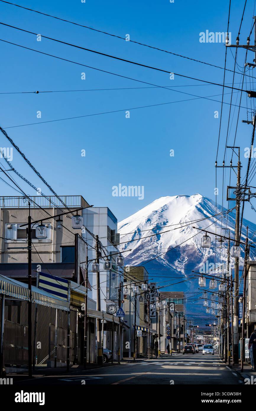 Il Monte Fuji innevato, visto da una tranquilla via dello shopping a Fujiyoshida, Yamanashi, Giappone. Il paesaggio urbano di tutti i giorni contrasta con la maestosa montagna Foto Stock