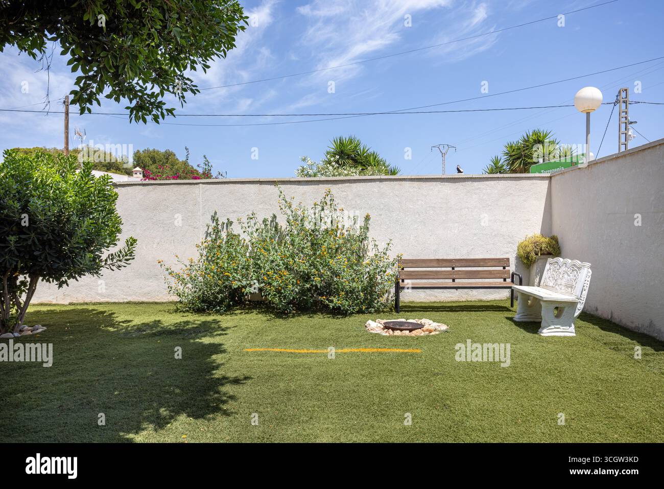 Angolo giardino tranquillo con panche in legno e cemento, caminetto e arbusti fioriti contro alte pareti. Foto Stock