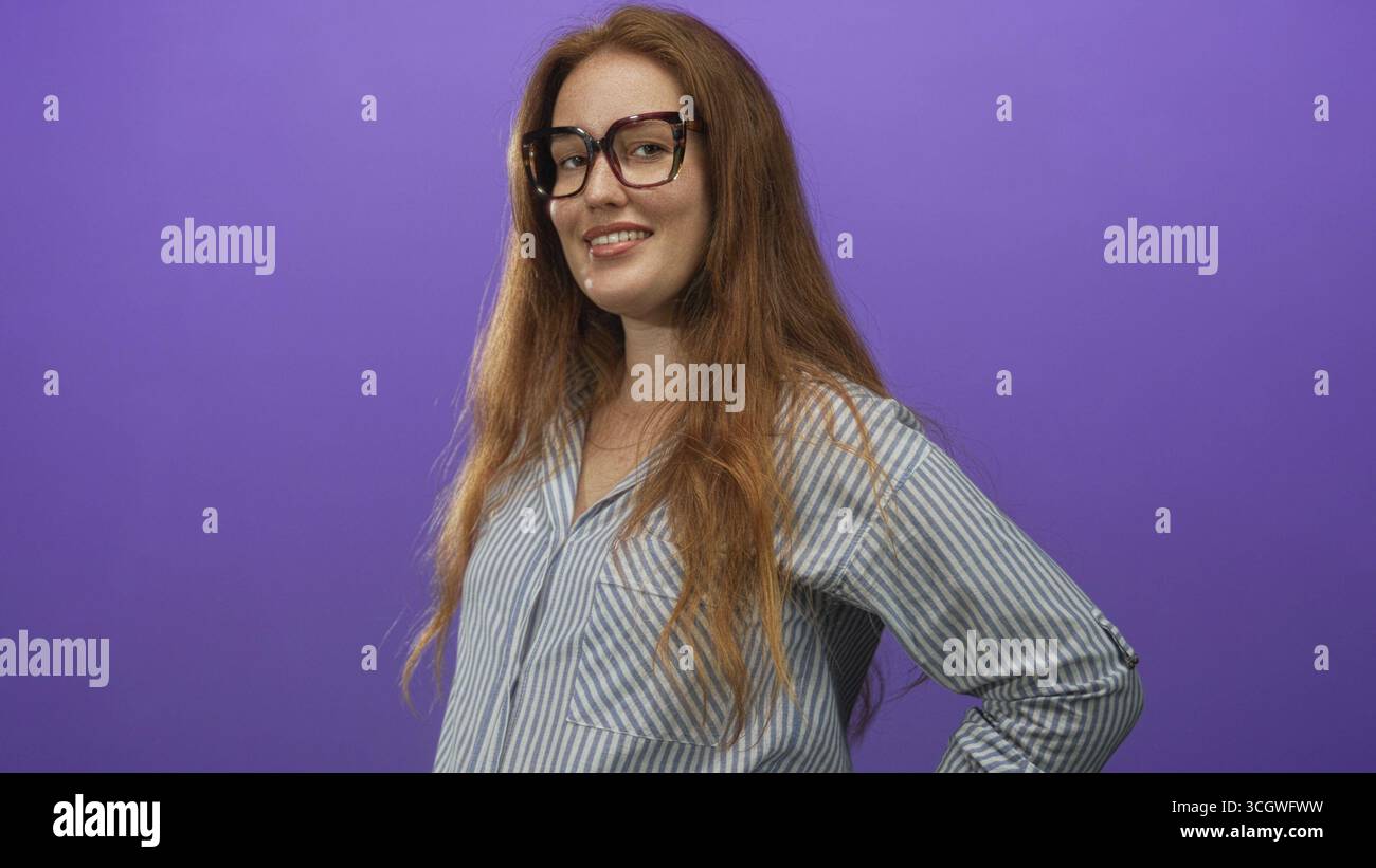 Donna che indossa gli occhiali regala le mani sui fianchi con un sorriso sottile contro la parete viola dello studio; sicurezza. Foto Stock