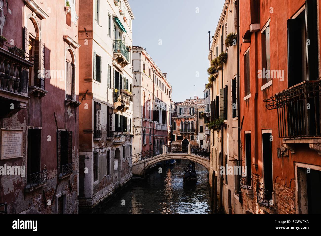 Stretto canale veneziano con gondola che passa sotto un piccolo ponte tra colorati edifici storici Foto Stock Stretto canale veneziano con gondola che passa sotto un piccolo ponte tra colorati edifici storici Foto Stock