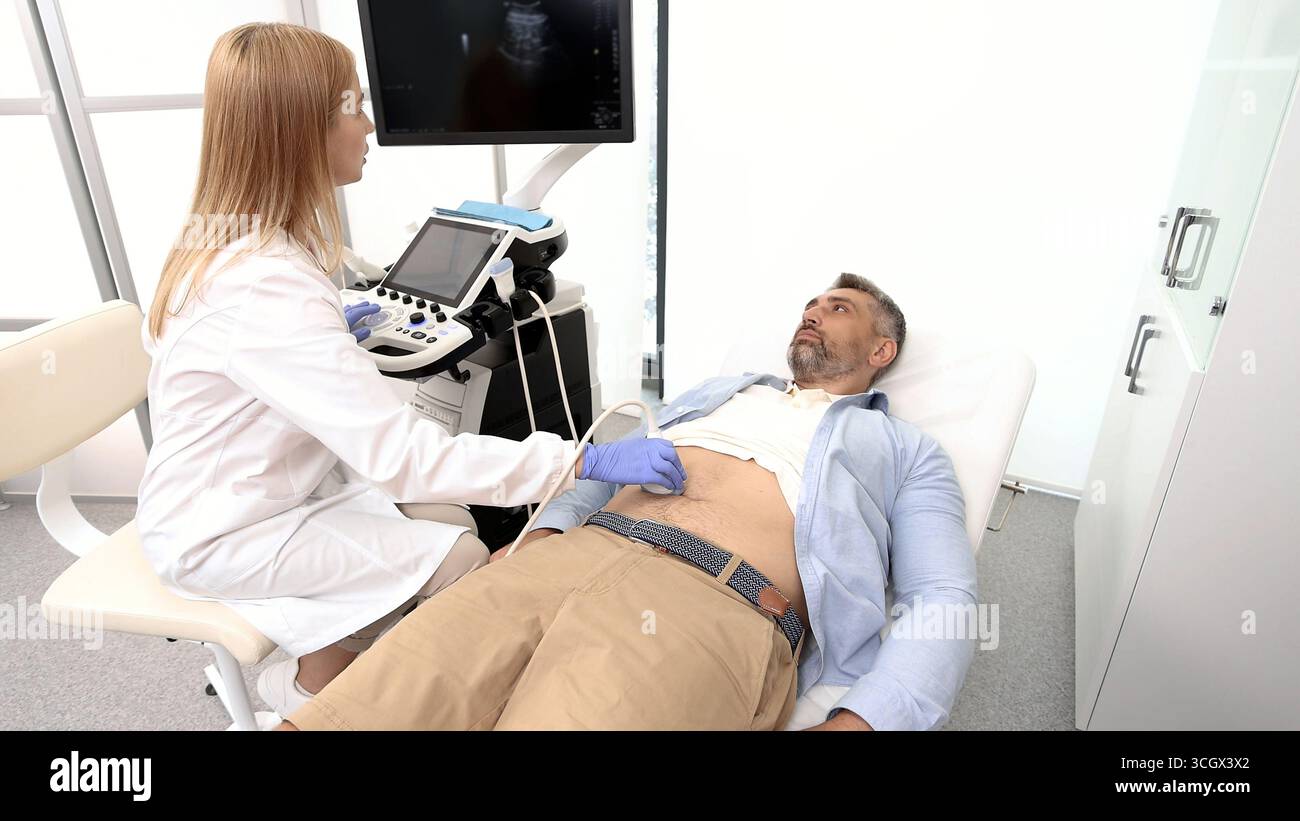 Specialista di ultrasuoni che fa l'ecografia della cavità addominale per il paziente di sesso maschile con la macchina a ultrasuoni in ospedale Foto Stock