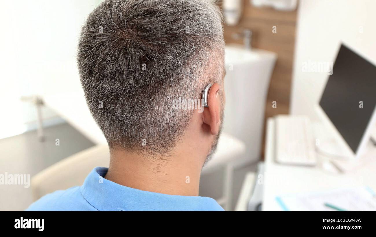 Un uomo maturo prova il suo apparecchio acustico dietro l'orecchio personalizzato mettendolo sull'orecchio. Soluzioni per l'udito per persone con problemi di udito Foto Stock