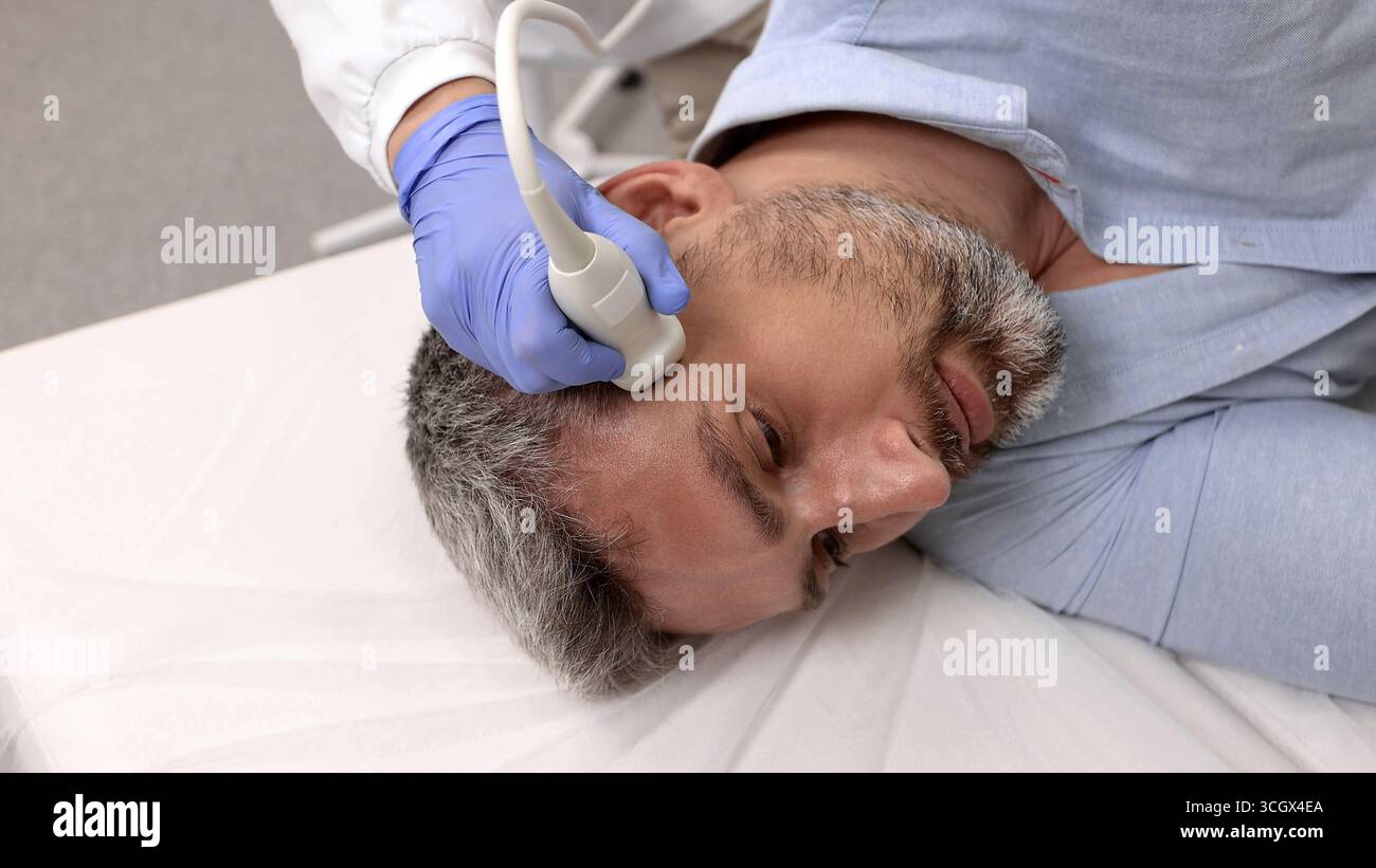 Specialista di ecografia esperto analizza attentamente la struttura dei vasi del collo di bel paziente utilizzando un moderno dispositivo sonografico in ospedale Foto Stock
