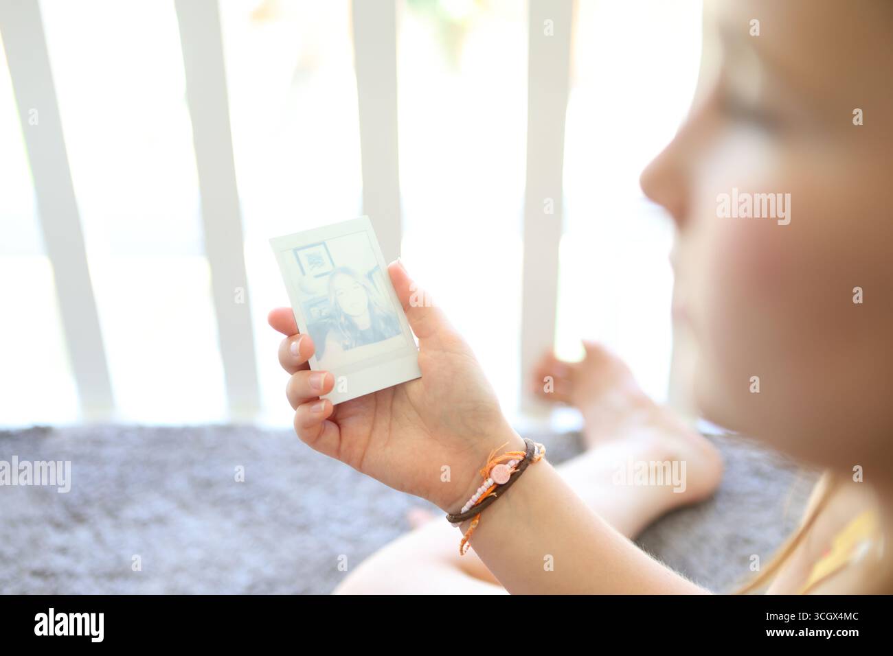 La ragazza tiene la stampa istantanea dalla fotocamera istantanea mentre la stampa sviluppa l'immagine Foto Stock