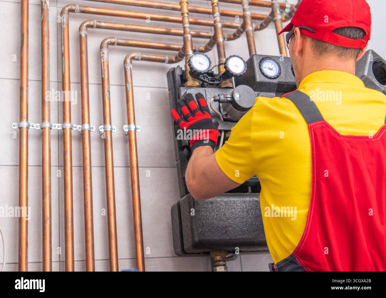 Un tecnico lavora diligentemente su un impianto idrico, controllando manometri e tubi in una moderna area residenziale per garantire il corretto funzionamento e la sicurezza. Foto Stock