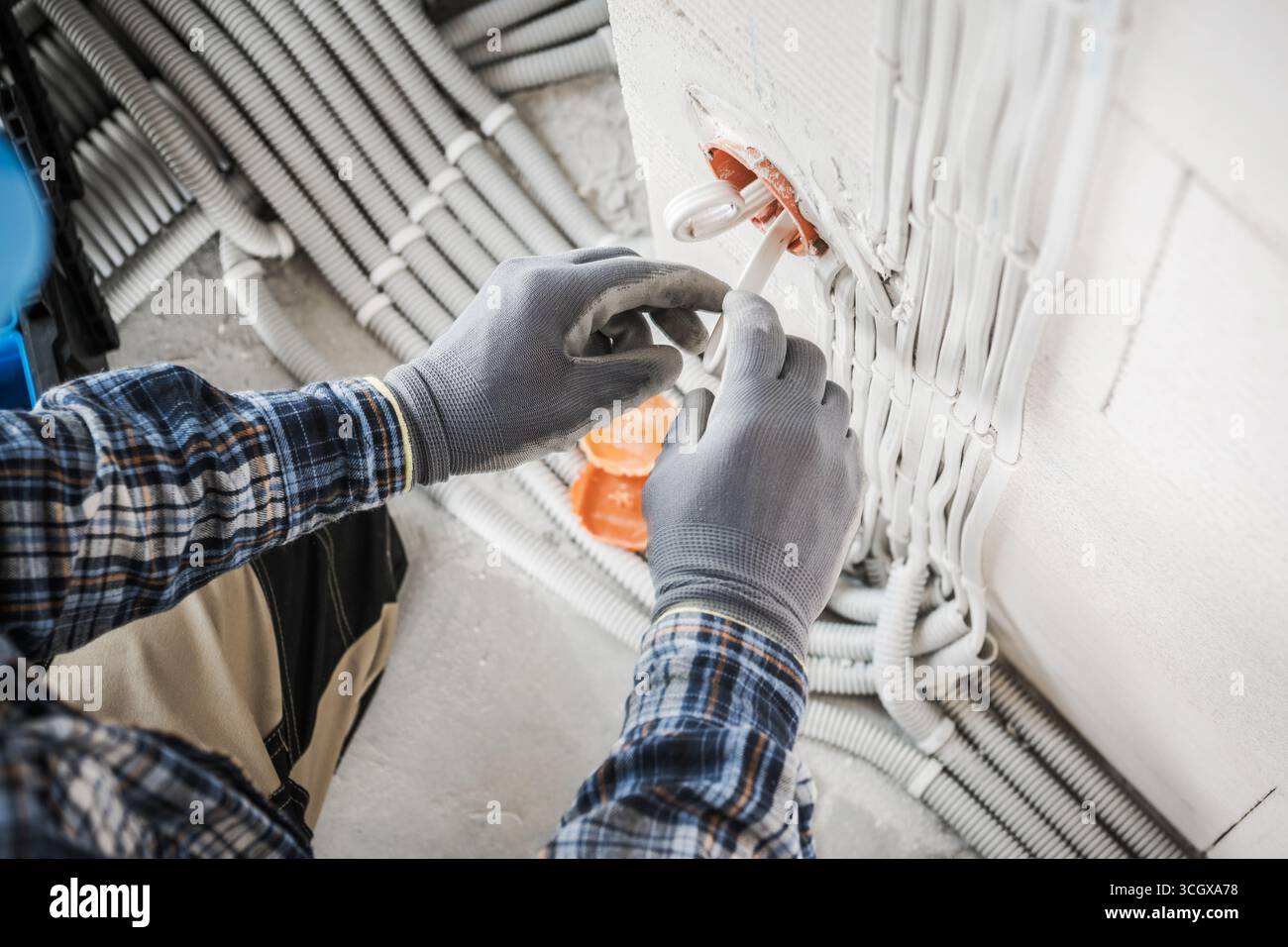 Un operatore con guanti collega il cablaggio elettrico in un edificio in costruzione, garantendo la corretta installazione dei componenti per la sicurezza e la funzionalità Foto Stock